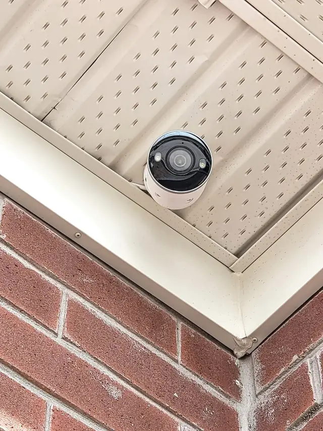 Dome security camera installed under the eaves of a red-brick home in Burlington